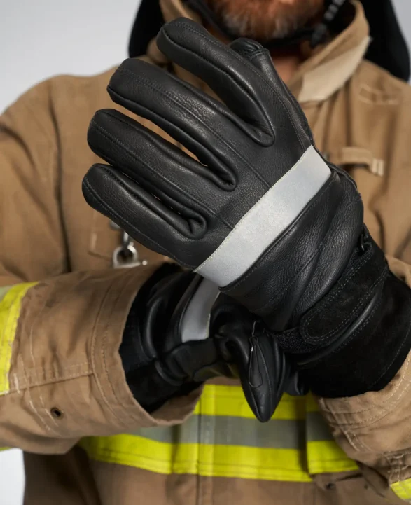 Unrecognizable bearded firefighter wearing black protective gloves. Crop view of male fireman putting on leather firefighting gloves, on white background. Concept of profession, fire equipment.